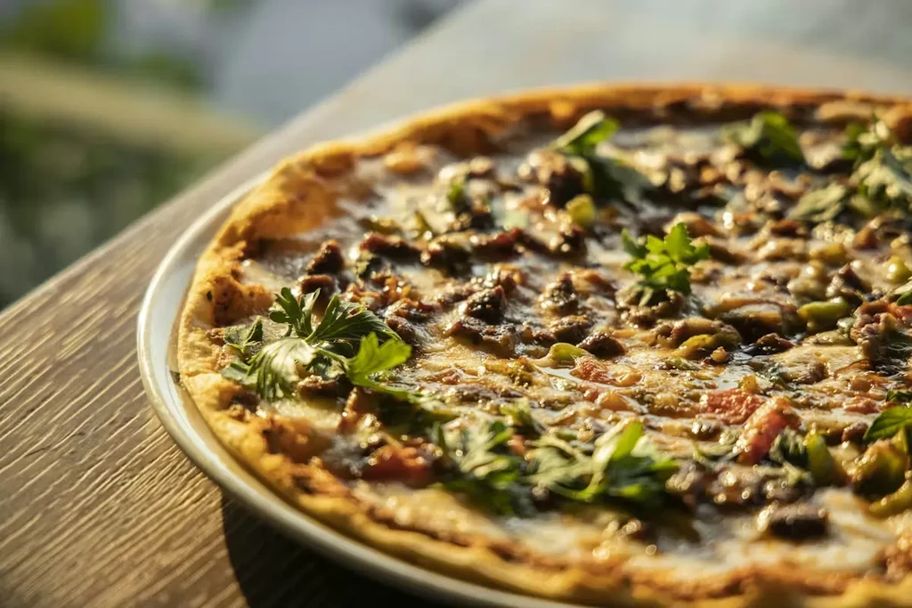 Close-up of pizza with ground meat, melted cheese, and fresh green herbs.