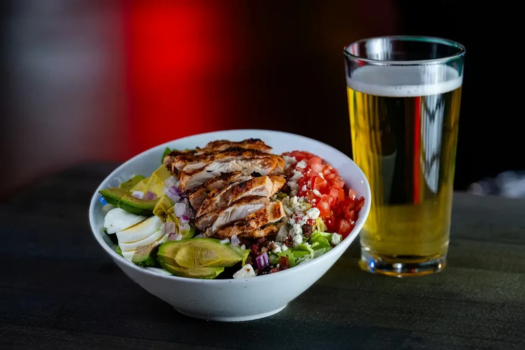 Grilled chicken salad and golden beer on a dark, glowing background.