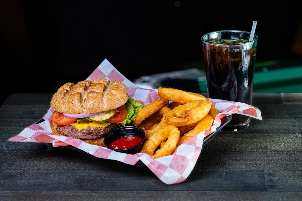 Cheeseburger, fries, onion rings, ketchup, and dark soda in a basket.