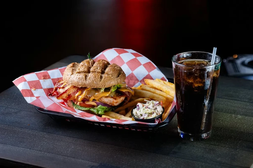 Large sandwich with grilled meat, fries, coleslaw, and soda.
