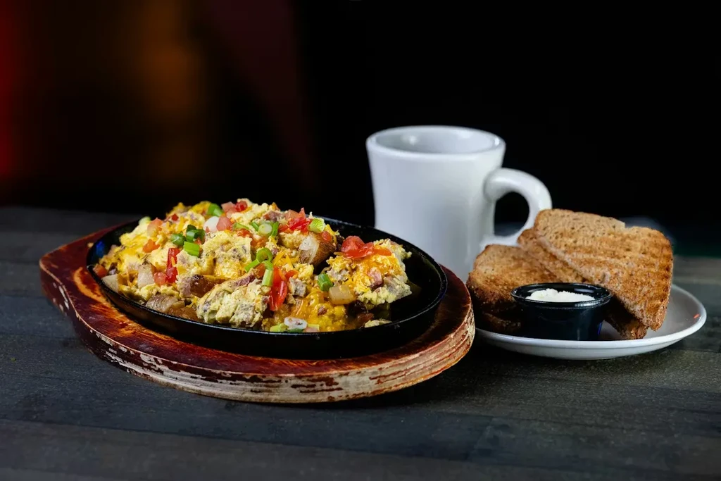Cast iron skillet with scrambled eggs, cheese, potatoes, toast, and coffee.