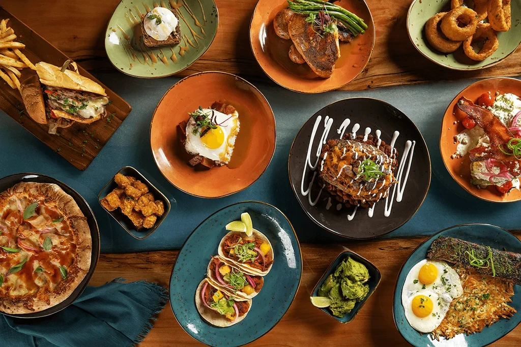 Overhead flat lay of diverse gourmet dishes on a wooden table.