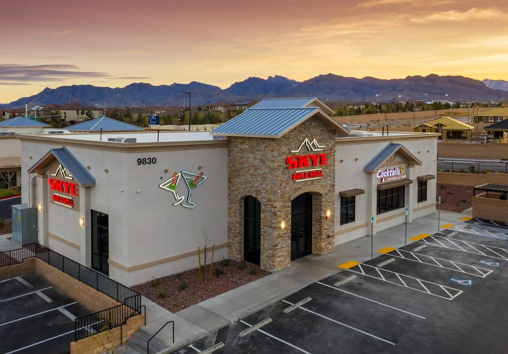 Modern SKYE BAR & GRILL exterior at sunset, empty parking lot, mountains.