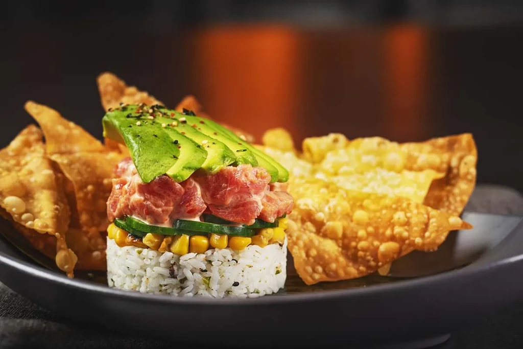 Layered tuna poke stack with avocado, rice, corn, and chips.