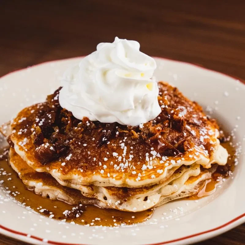 Stack of three pancakes with caramel, whipped cream, and powdered sugar.