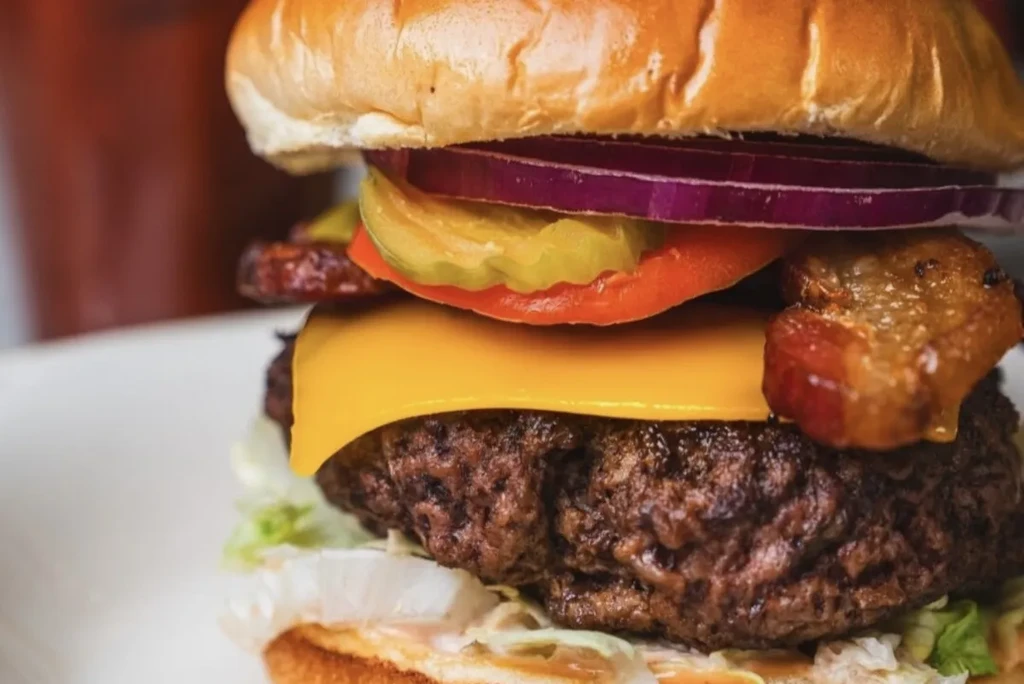 Layered cheeseburger with beef patty, melted cheese, bacon, and fresh vegetables.