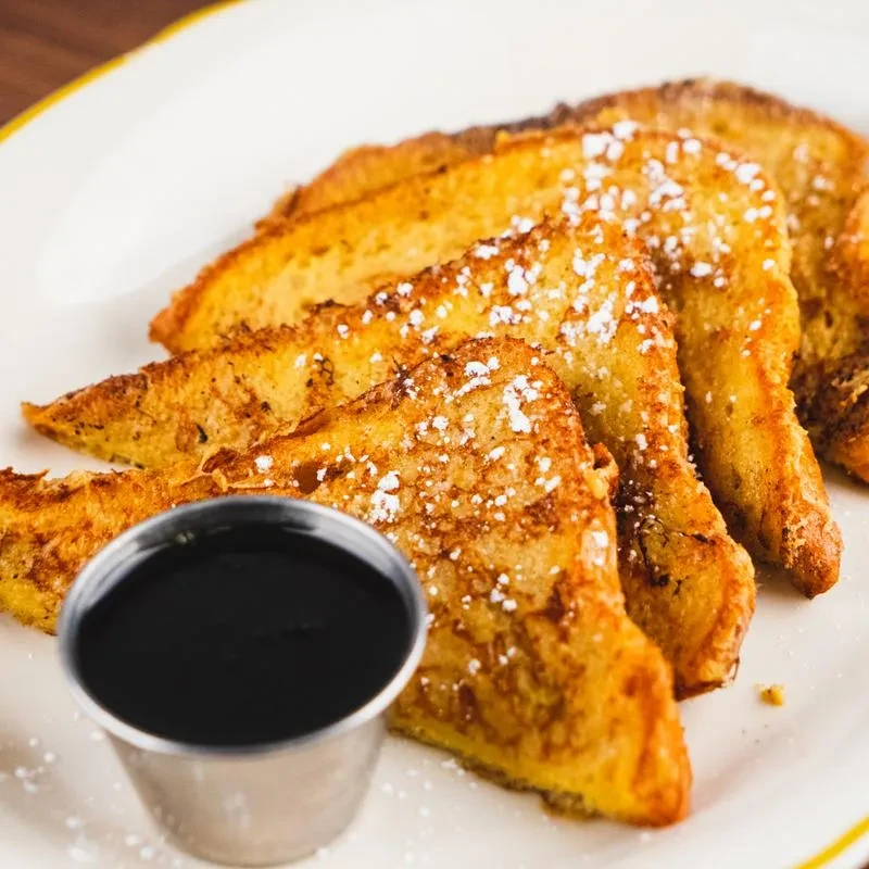 Triangular golden French toast, powdered sugar, and side of maple syrup.
