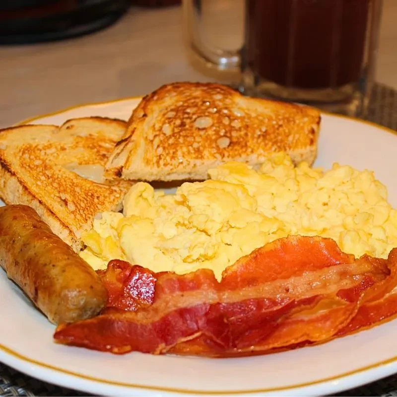A classic breakfast plate with sausage, bacon, scrambled eggs, and toast.