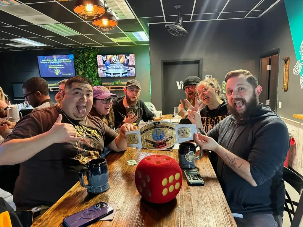Six people posing with a wrestling belt and dice at a pub.