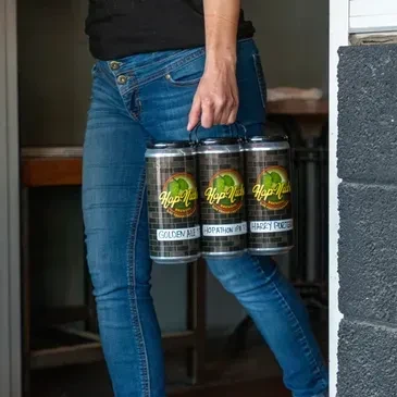Person walking, carrying a 6-pack of Hop-Nut Brewing beer cans.