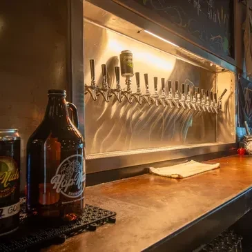 Row of metallic beer taps above a 'Hop Nuts' growler on a bar.