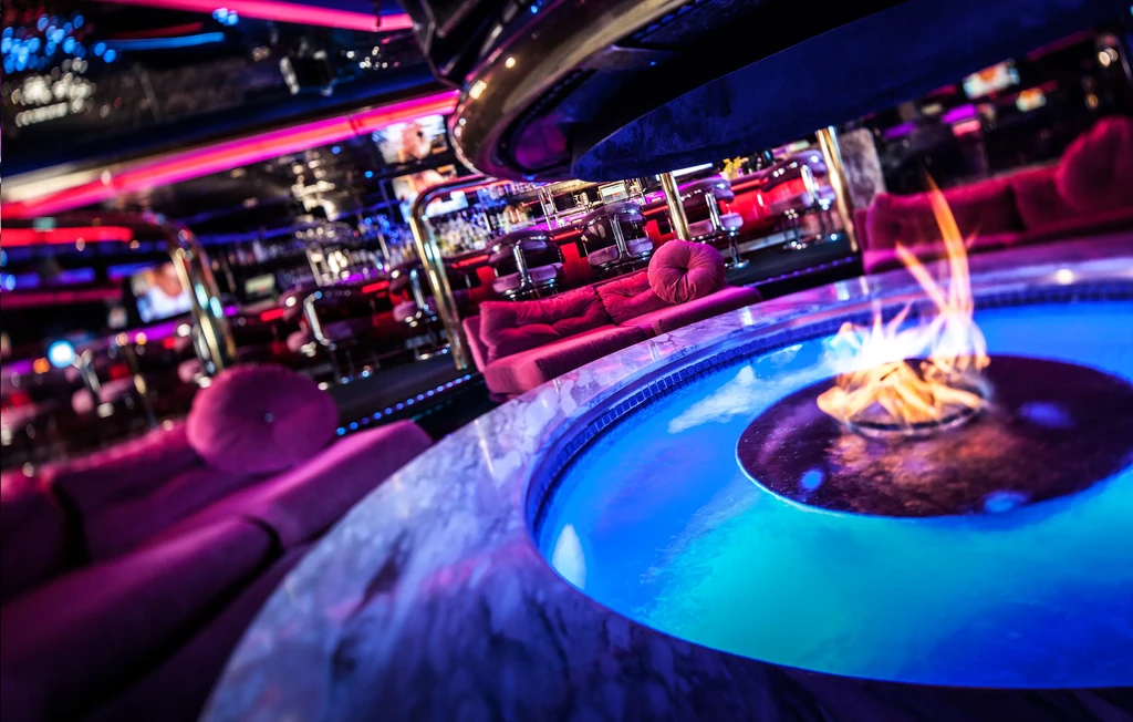 Luxurious lounge with blue-lit water feature, fire pit, and red sofas.