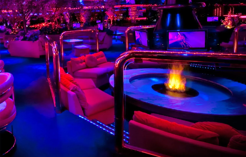 Neon-lit modern lounge with blue water, pink seating, and fire pit.
