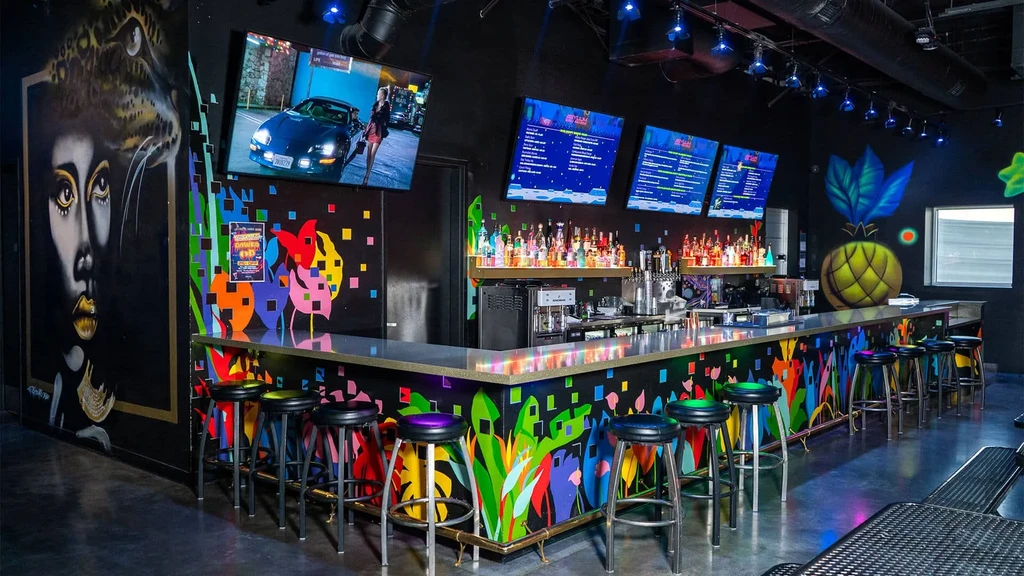 Lively bar interior with colorful murals, wall graffiti, and glowing bottles.