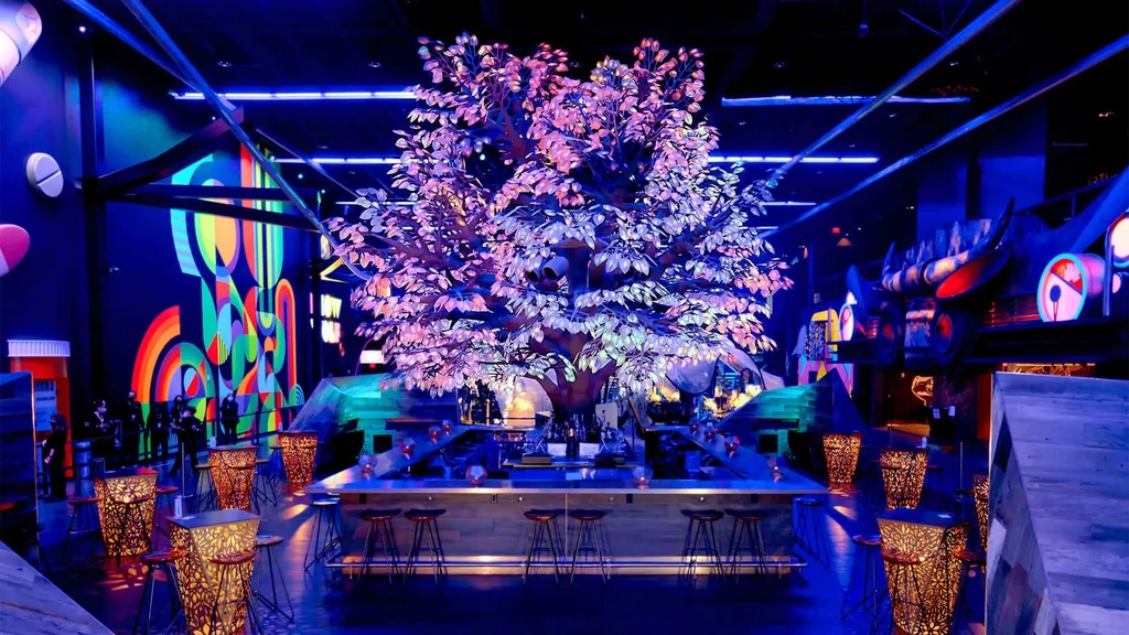 Modern bar with glowing purple tree, neon mural, and pill-shaped decor.