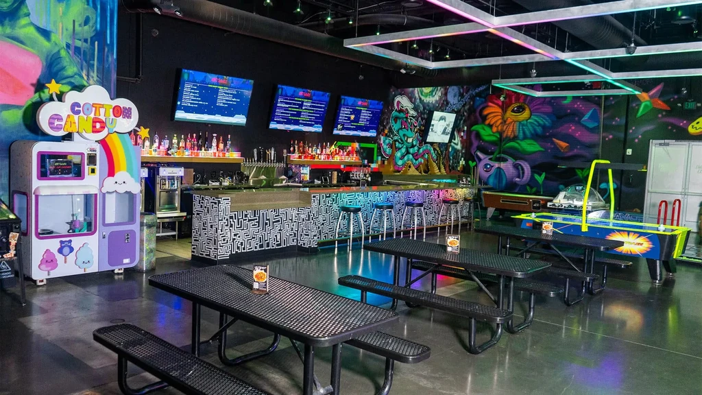 Colorful bar-arcade interior with graffiti walls, a geometric bar, and games.