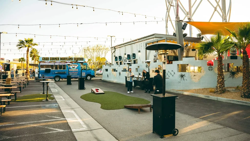 Outdoor food truck park with picnic tables, cornhole games, and string lights.