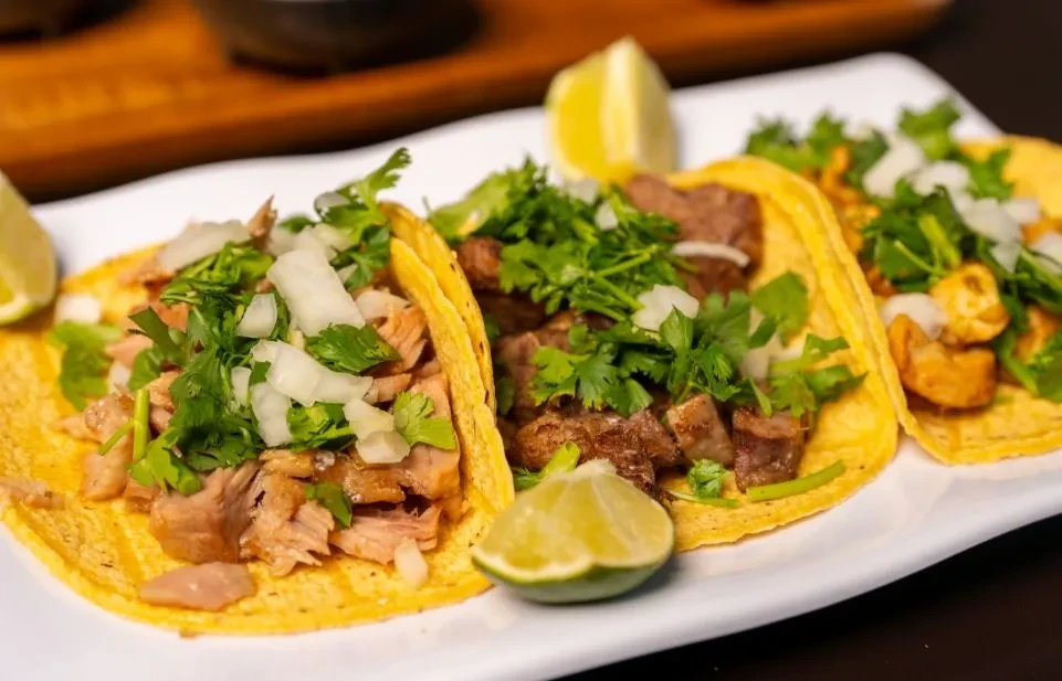 Three tacos with meat, onions, cilantro, and lime on a white plate.