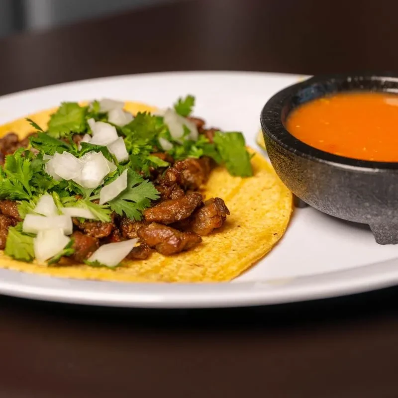 Close-up of one street-style taco with meat, onions, cilantro, and salsa.