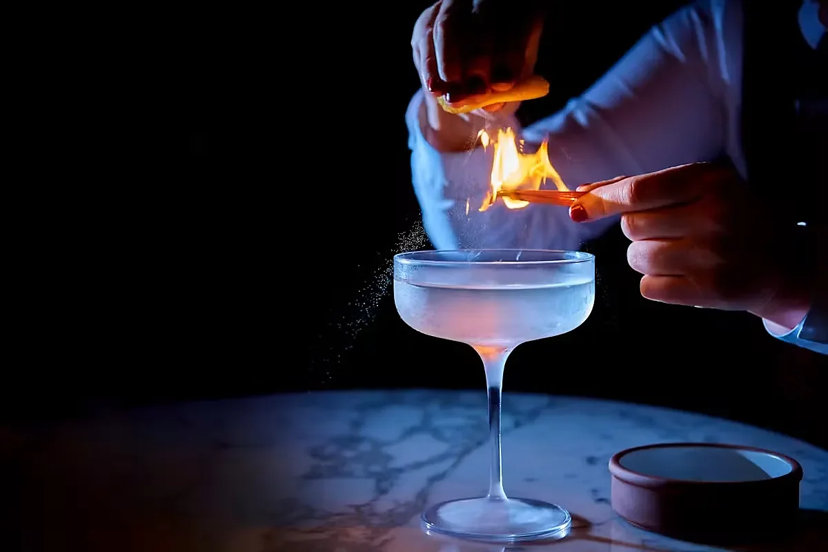Bartender flaming an orange peel over a coupe cocktail