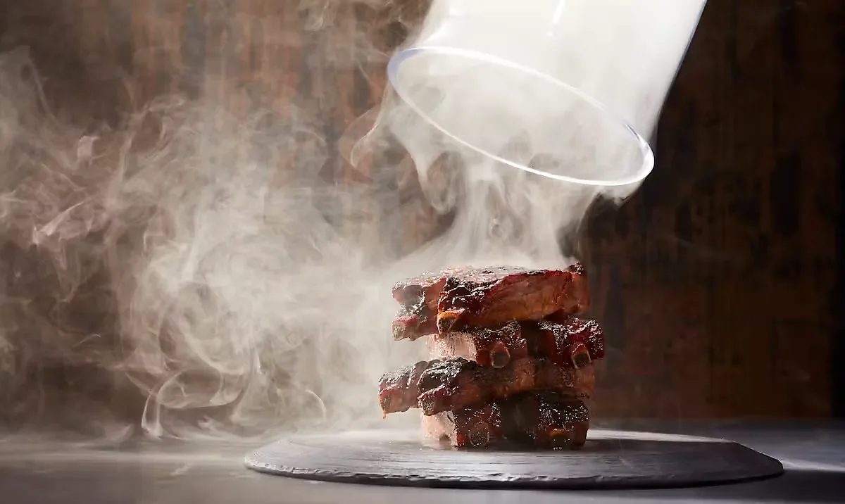 Stack of barbecue ribs on slate with smoke being released