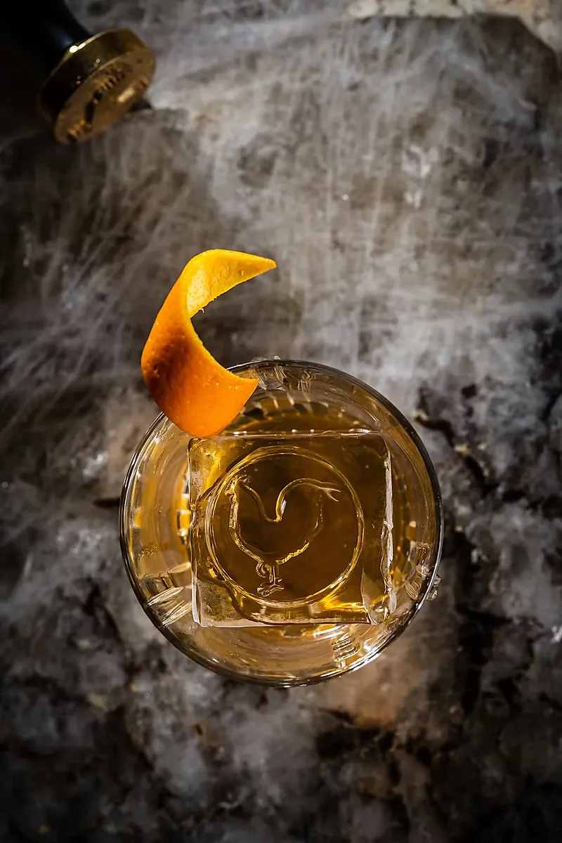 Overhead bourbon cocktail with orange twist and rooster-etched ice cube