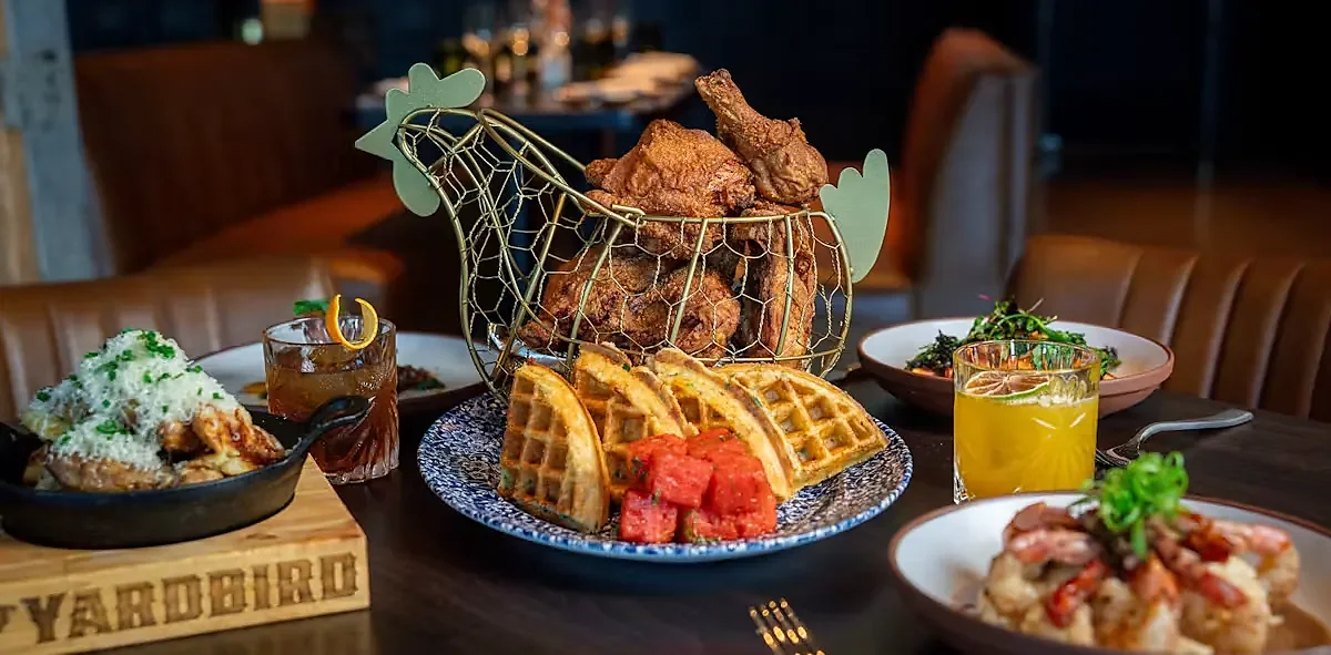 Table spread of fried chicken, waffles, sides and two cocktails