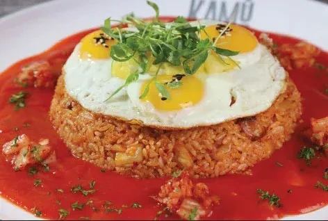 Kimchi fried rice with four sunny-side-up eggs, microgreens, and red sauce.