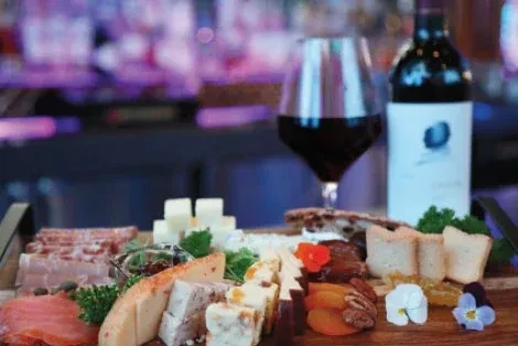 Charcuterie and cheese board with wine, meats, salmon, and blurred background.