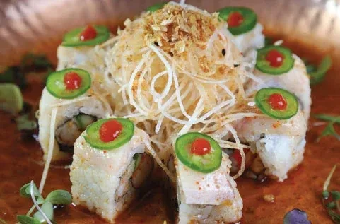Platter of sushi rolls topped with jalapeño, red sauce, and garnishes.