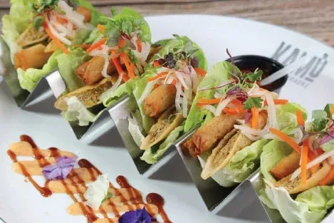Five lettuce wraps in stands with fried items, vegetables, sauces.