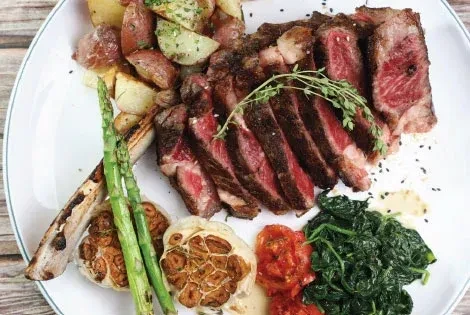 Medium-rare sliced steak, roasted potatoes, asparagus, tomatoes, spinach, and garlic.