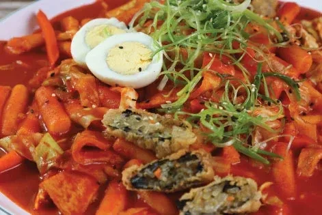 Tteokbokki with rice cakes, gimmari, hard-boiled egg, and green onions.
