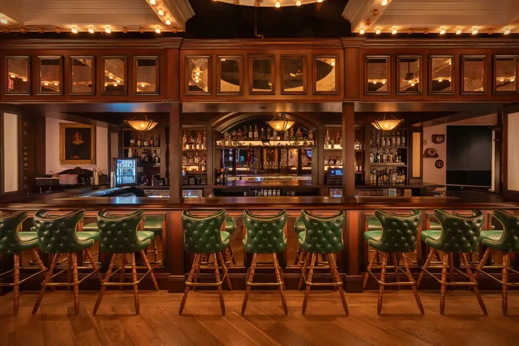 Empty classic bar with wooden counter, green stools, and stocked back bar.