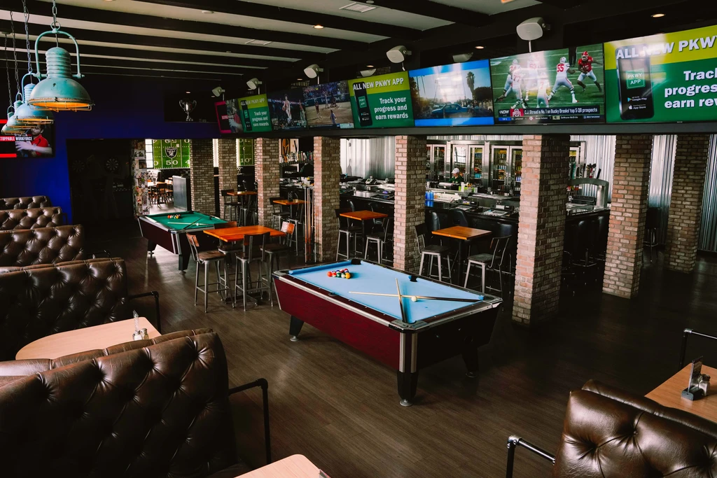 Modern sports bar interior with pool tables, a bar, and multiple TVs.
