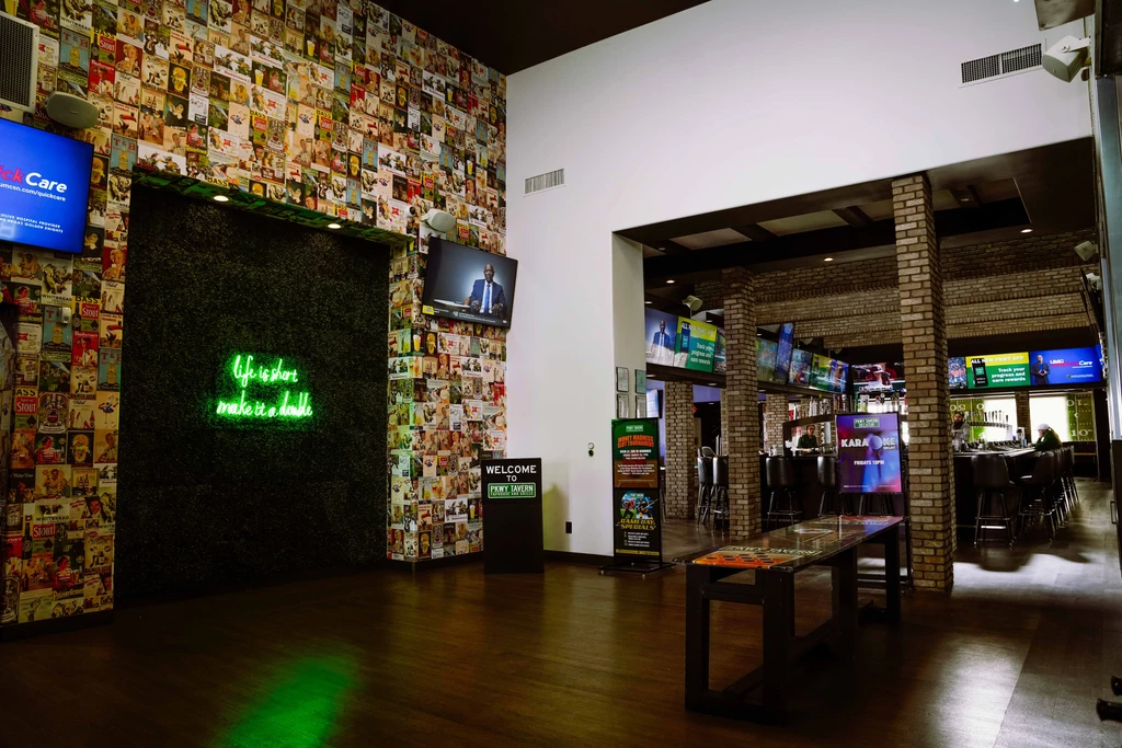 PNNY TAVERN interior with vintage poster wall, neon sign, and brick bar.