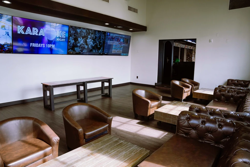 Modern lounge with leather seating, four TVs showing sports and karaoke.