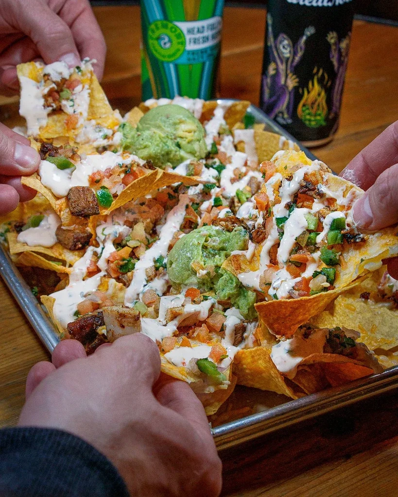 Multiple hands reach for loaded nachos topped with cheese and guacamole.