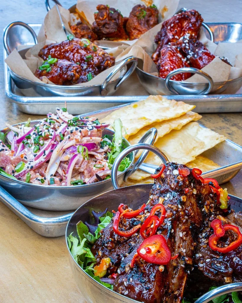 Colorful food spread with poke, ribs, and saucy chicken wings.