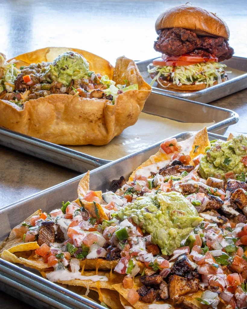 Nachos, taco salad, and a fried chicken sandwich on metal trays.