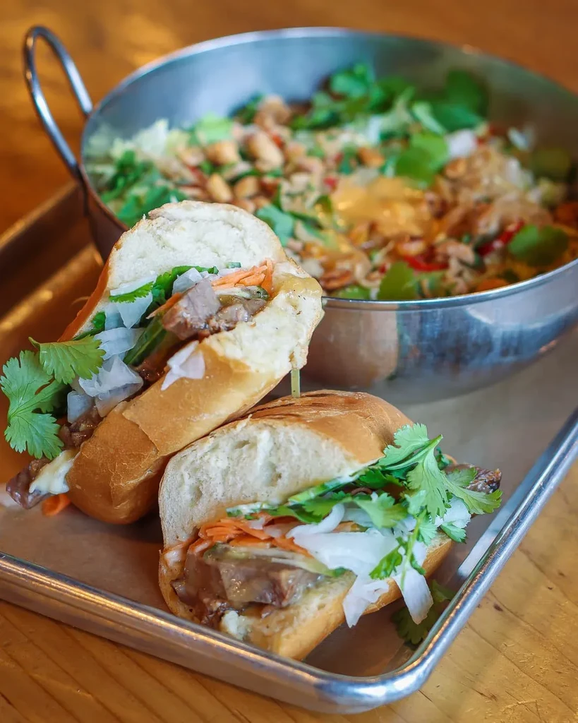 Two banh mi halves filled with meat, pickled vegetables, and cilantro.