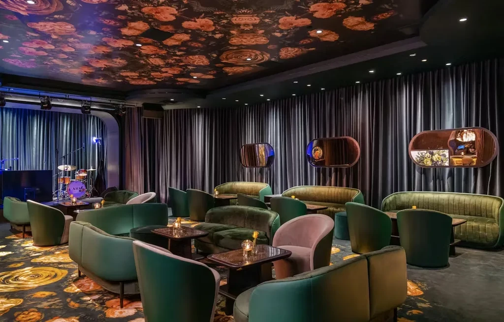 Dimly lit lounge with dark floral ceiling, drapes, stage, and seating.