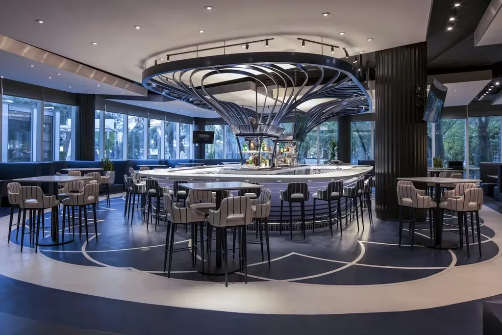 Modern restaurant interior: oval central bar, dark sculptural canopy.