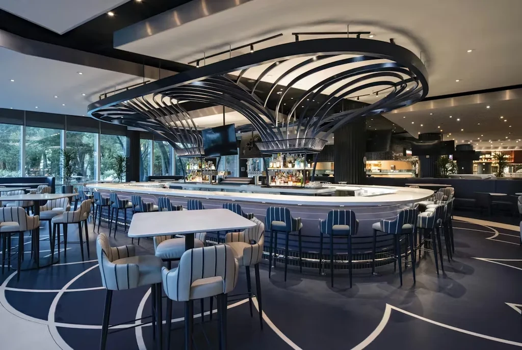 Modern bar interior with oval bar, stools, and sculptural ceiling fixture.
