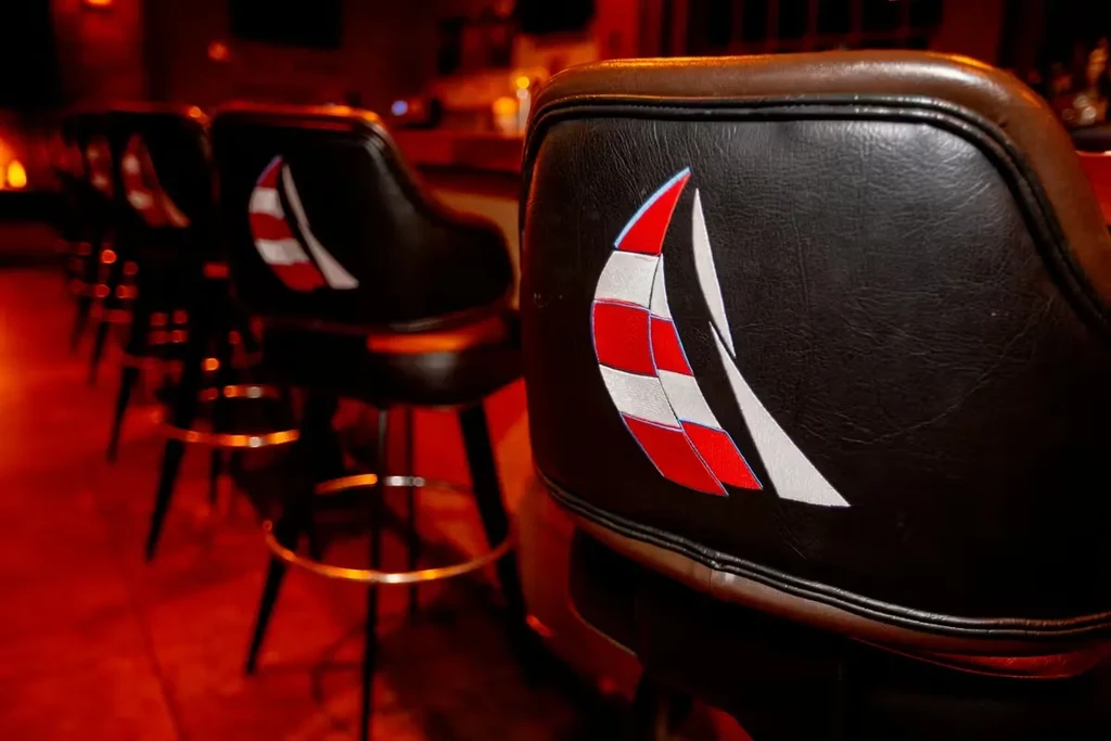 Row of dark bar stools with a red/white emblem in a dimly lit bar.