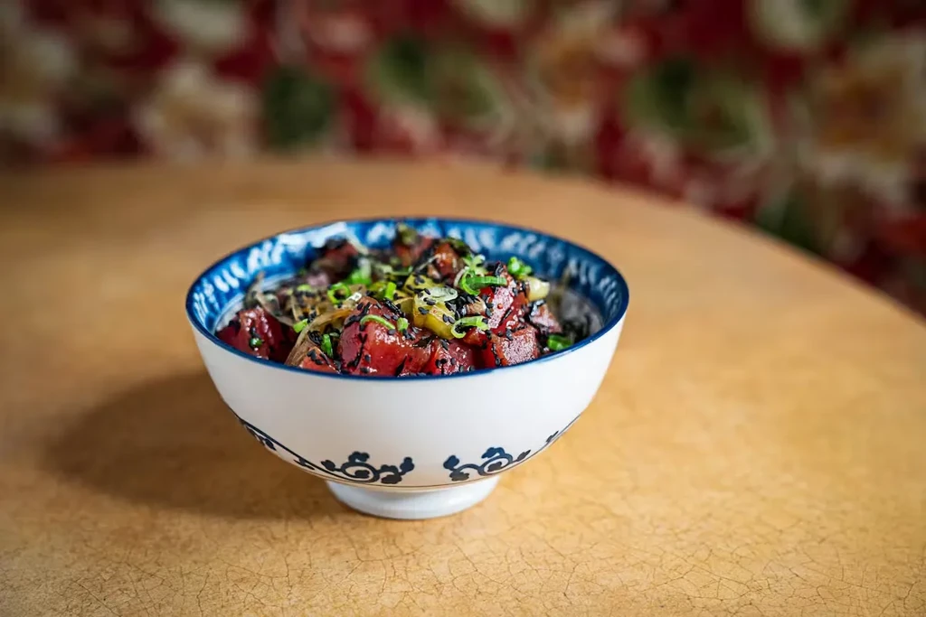 White ceramic bowl of tuna poke with green onions and black sesame.