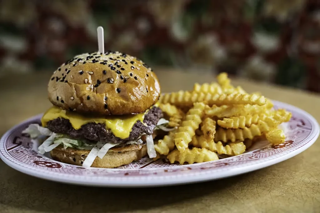 Burger with sesame bun, melted cheese, lettuce, and crinkle-cut fries.