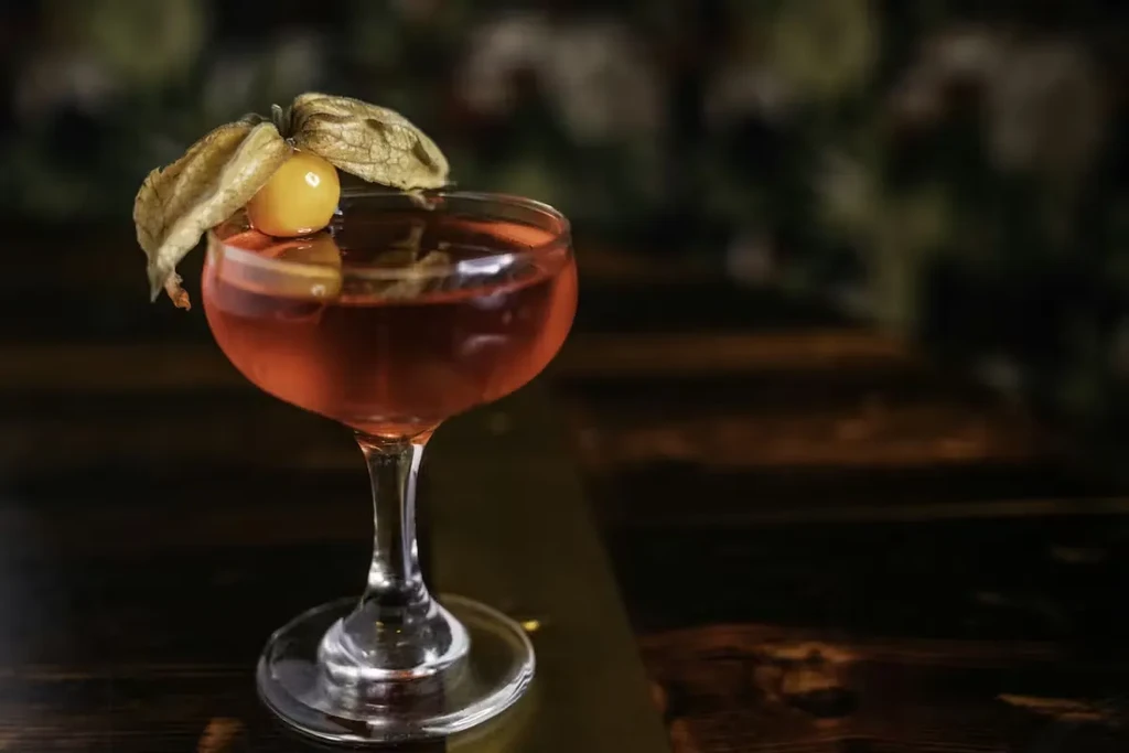 Reddish-brown cocktail in a coupe glass with goldenberry garnish.