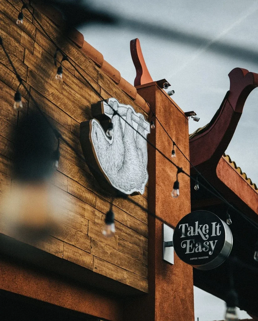Cafe facade with wooden panels, terracotta wall, sloth logo, and lights.