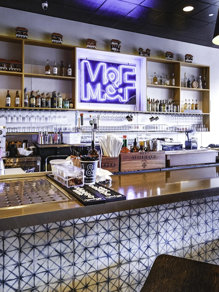 Modern bar counter with tiled front, liquor shelves, and purple M&M sign.